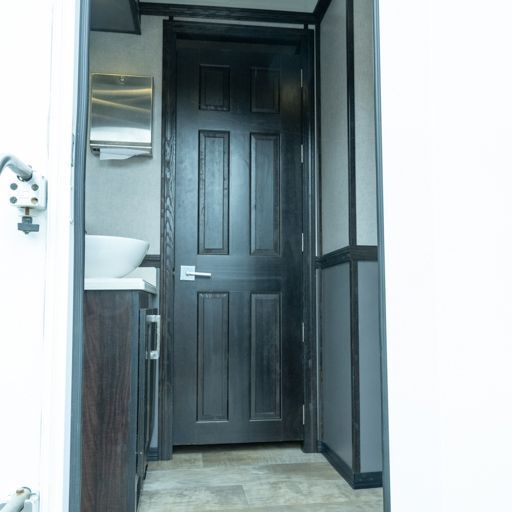 Narrow bathroom doorway with a dark wood door, white walls, and a small sink visible inside