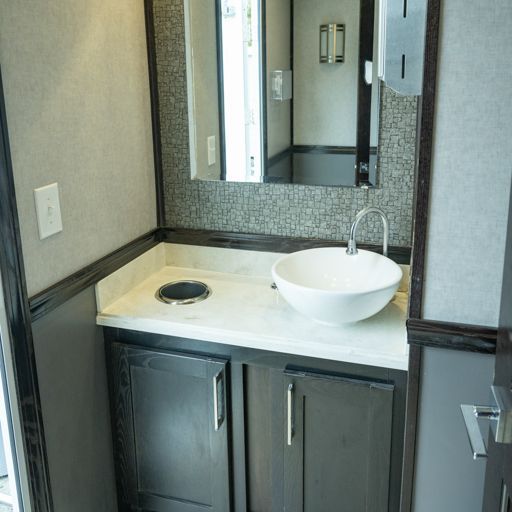 Modern bathroom vanity with white countertop, vessel sink, and dark cabinets beneath a wall mirror.