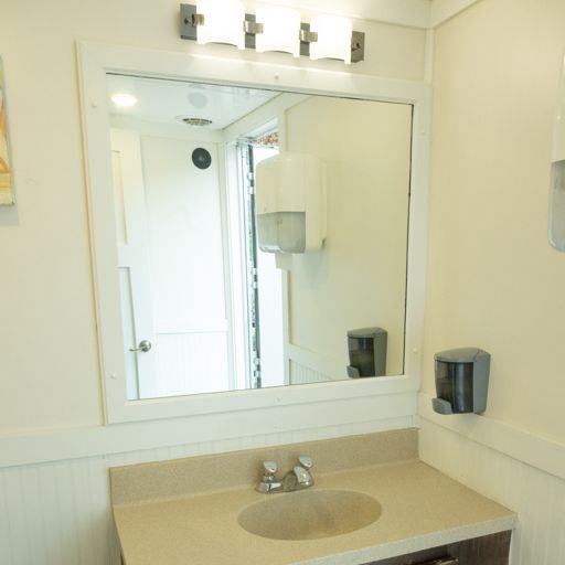 Small bathroom vanity with beige countertop, round sink, and large mirror reflecting a shower and toilet.