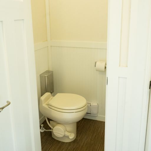 Small white toilet in a narrow beige bathroom stall with a toilet paper holder on the wall.