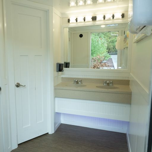 Small bathroom with white vanity, mirror lights, and a window view of greenery.