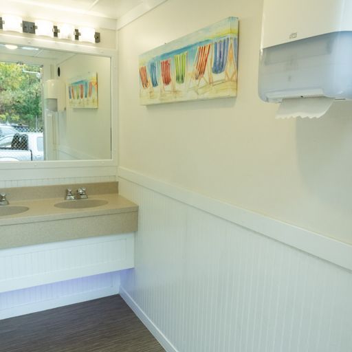 Bright restroom with sink, mirror, white wainscoting, wall art, and a paper towel dispenser.