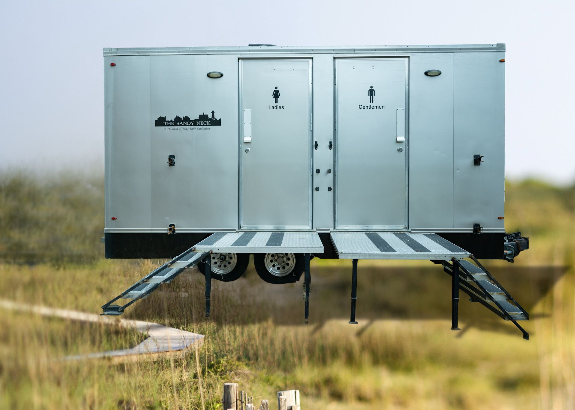 Metal mobile trailer with open ramps in a grassy field under an overcast sky