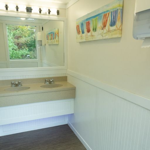 Bright bathroom vanity with double sinks, large mirror, white wainscoting, and colorful wall art.