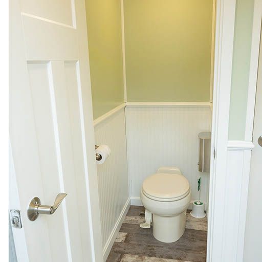 Small bathroom with a toilet, white beadboard walls, and green upper walls; door partly open.