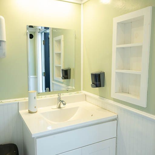 White bathroom vanity with sink, mirror, soap dispenser, and recessed wall shelves.