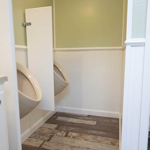Accessible restroom with two urinals and a partially open stall door, green and white walls, wood-look floor