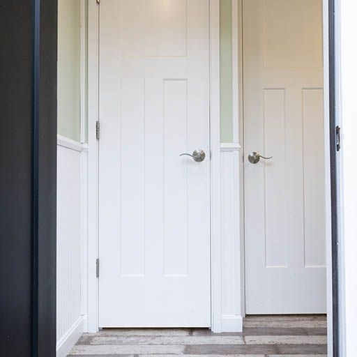 White hallway with two closed doors and silver handles beside gray trim and hardwood floor