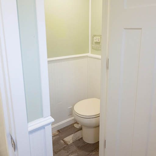 Small bathroom with an open door, white wainscoting, and a toilet in the corner.