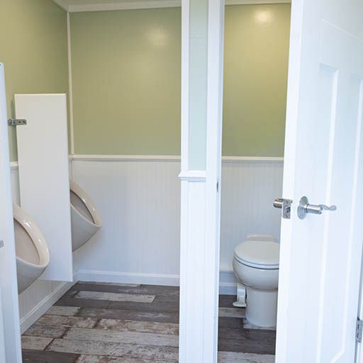 Small public restroom with white stalls, toilet, urinal, and pale green walls.