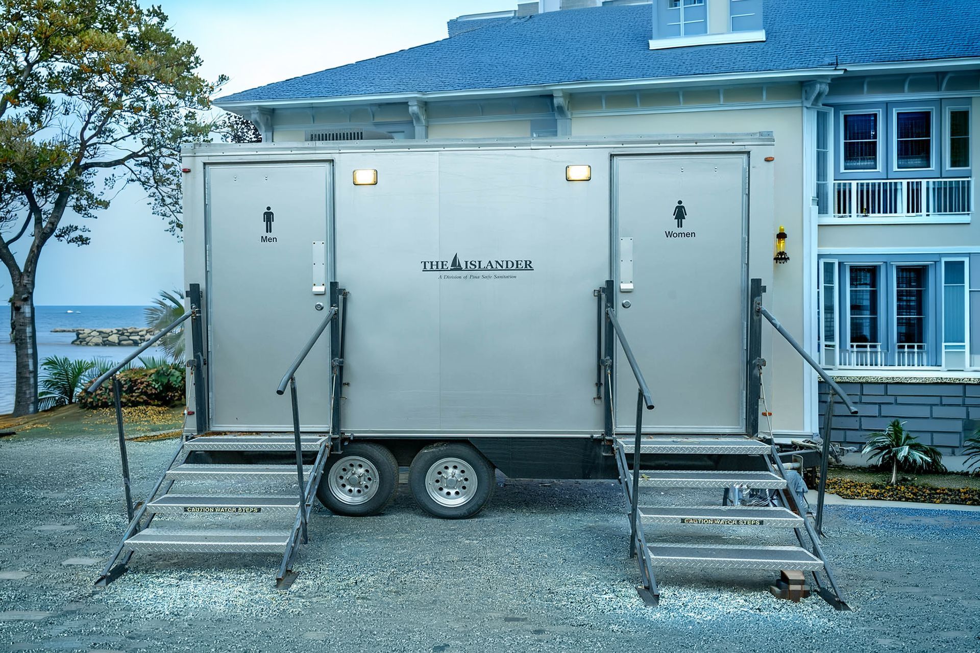 Portable restroom trailer with stairs, parked outside a building near the water.
