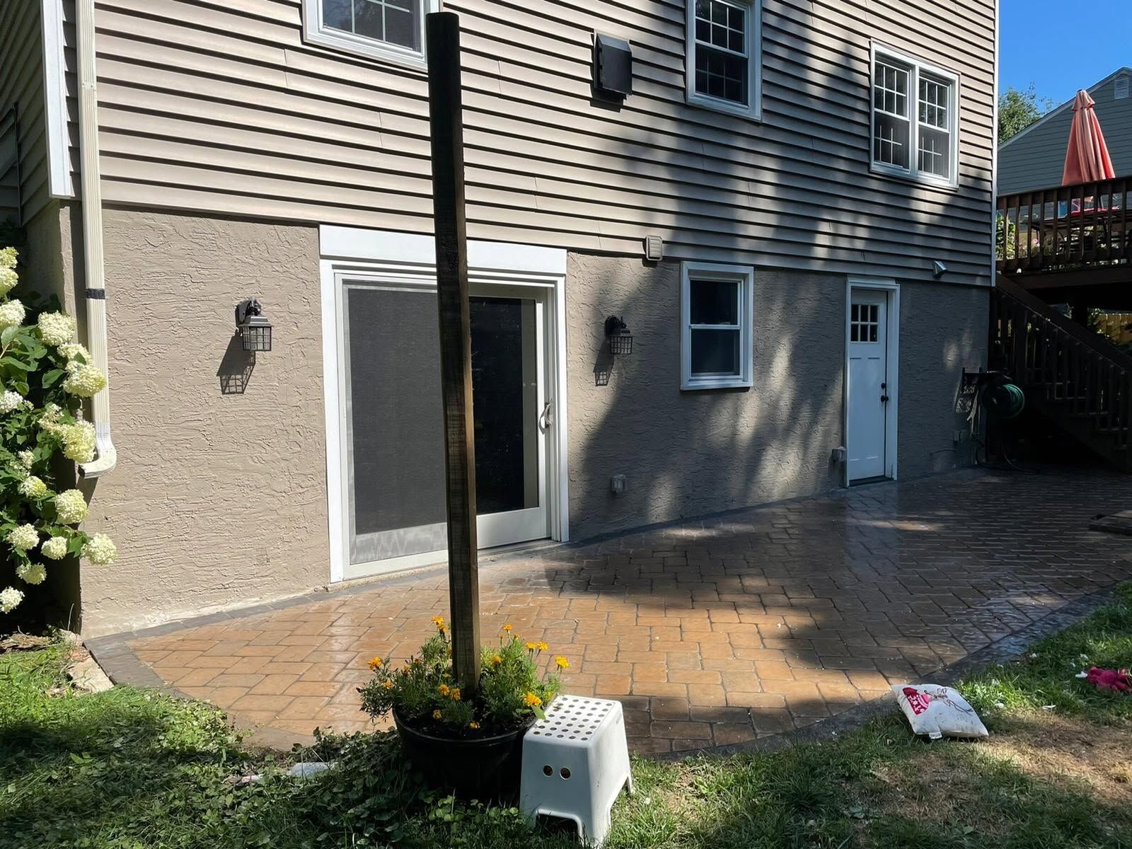 Back patio with wet brick pavers, beige house siding, sliding door, white door, and a small flower pot.