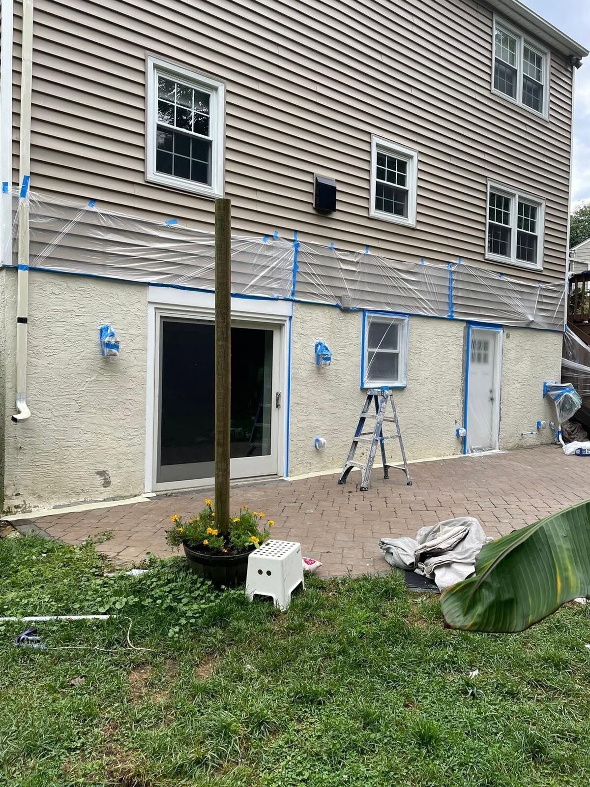 Backyard with house siding, open door, ladder, and fresh brick patio work area.