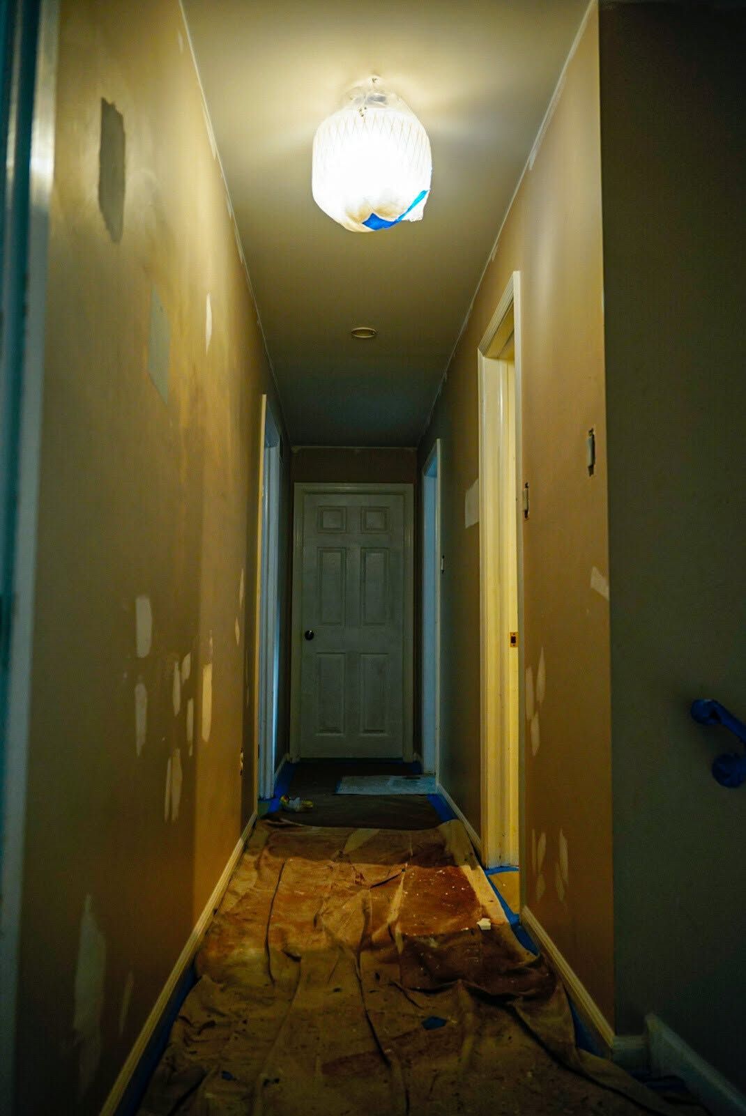 Narrow hallway with worn carpet, yellow walls, and a white door at the end under a ceiling light.