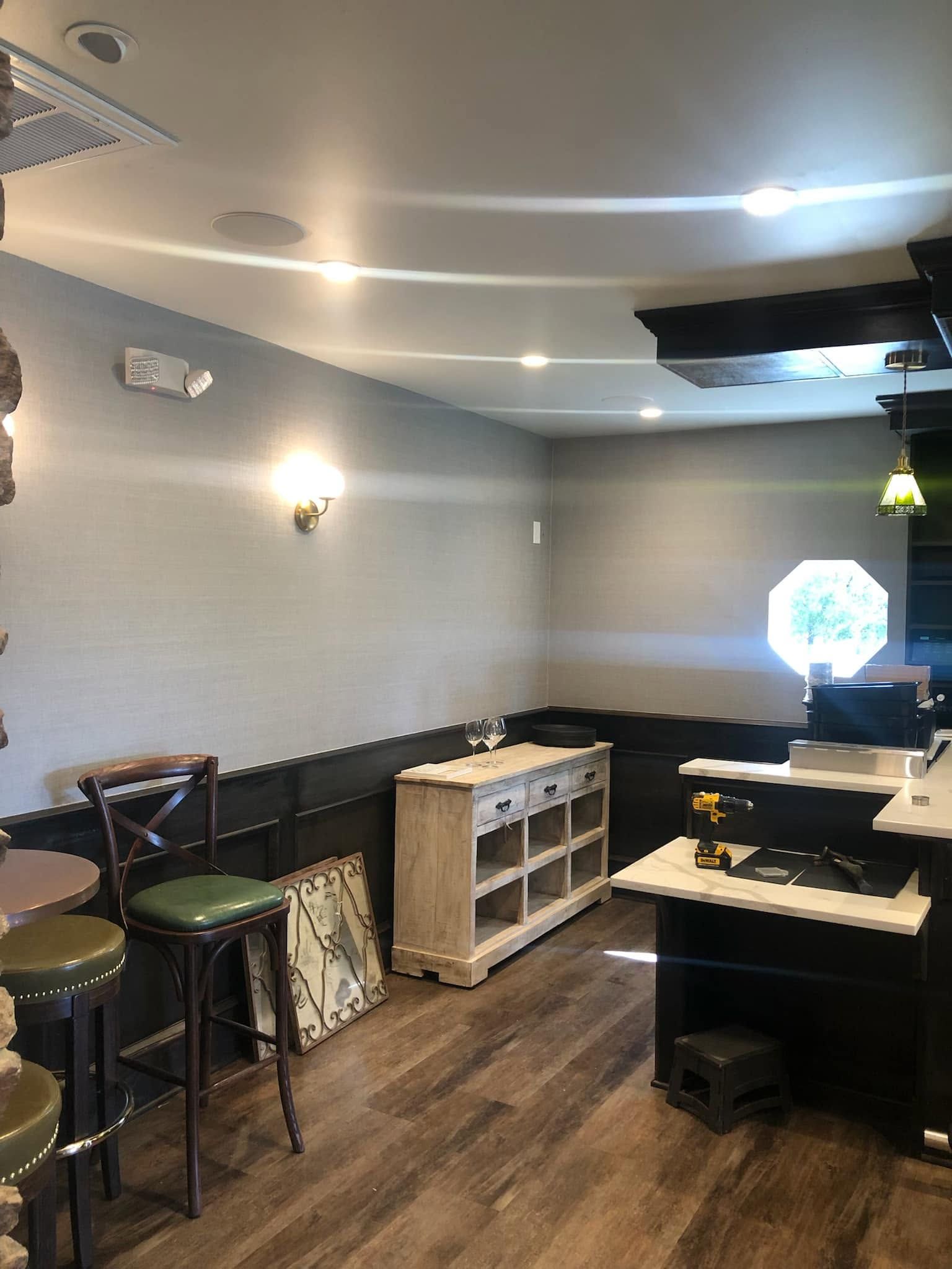 Empty café-like room with tables, stools, and gray walls under ceiling lights