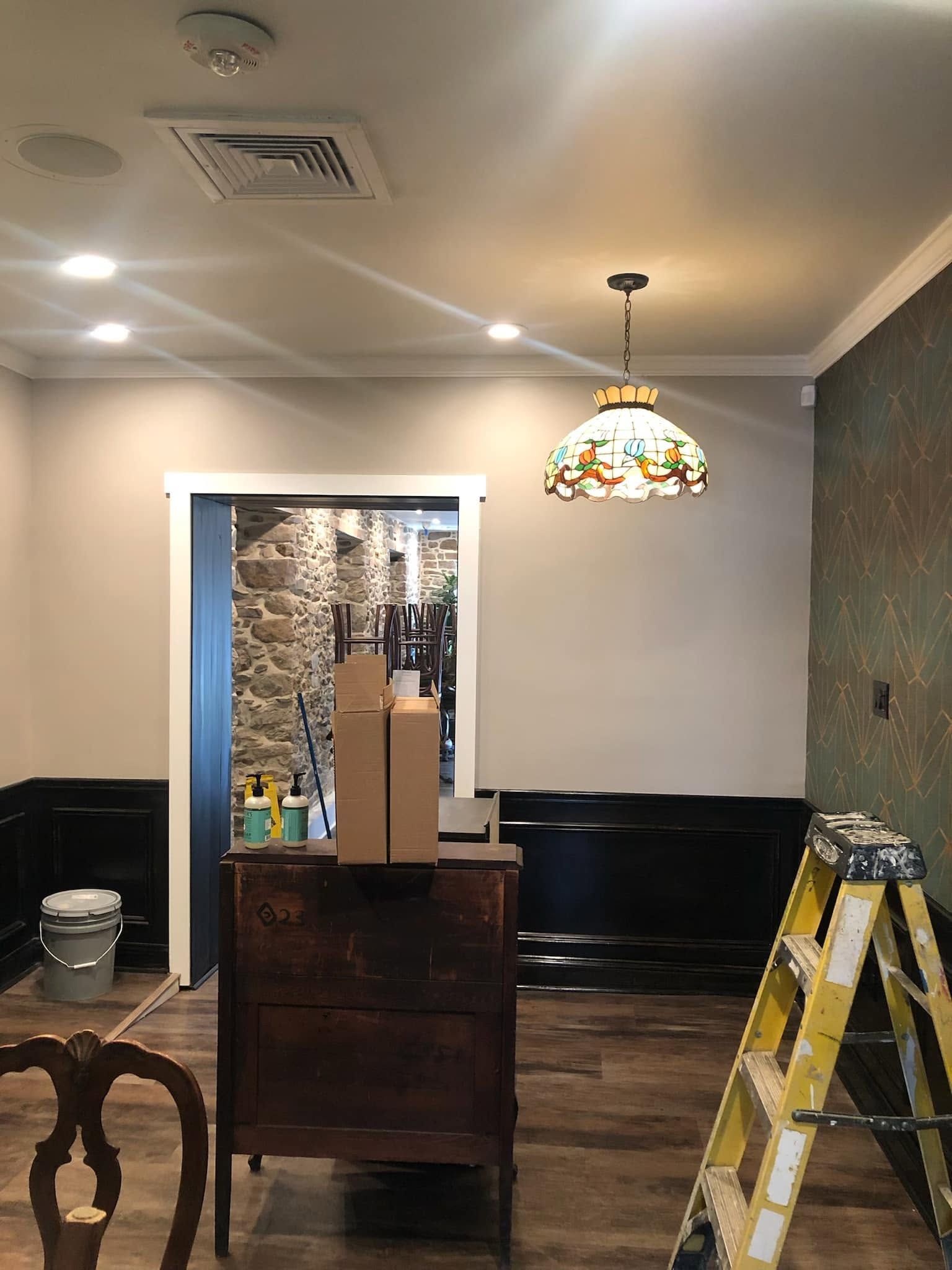 Living room under renovation with ladder, cabinet, ceiling light, and supplies on the floor