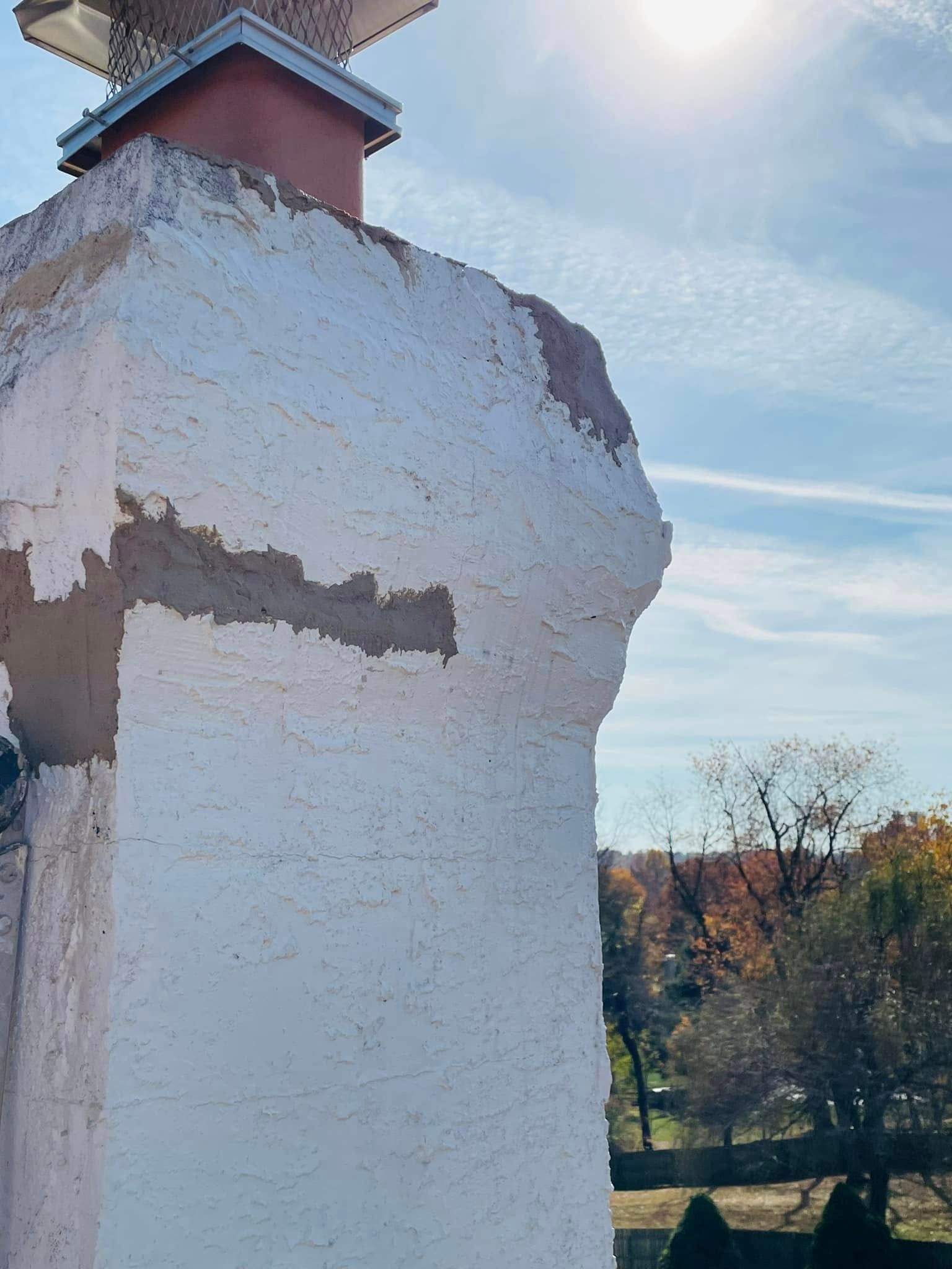 White weathered chimney with red cap against sunny blue sky and trees