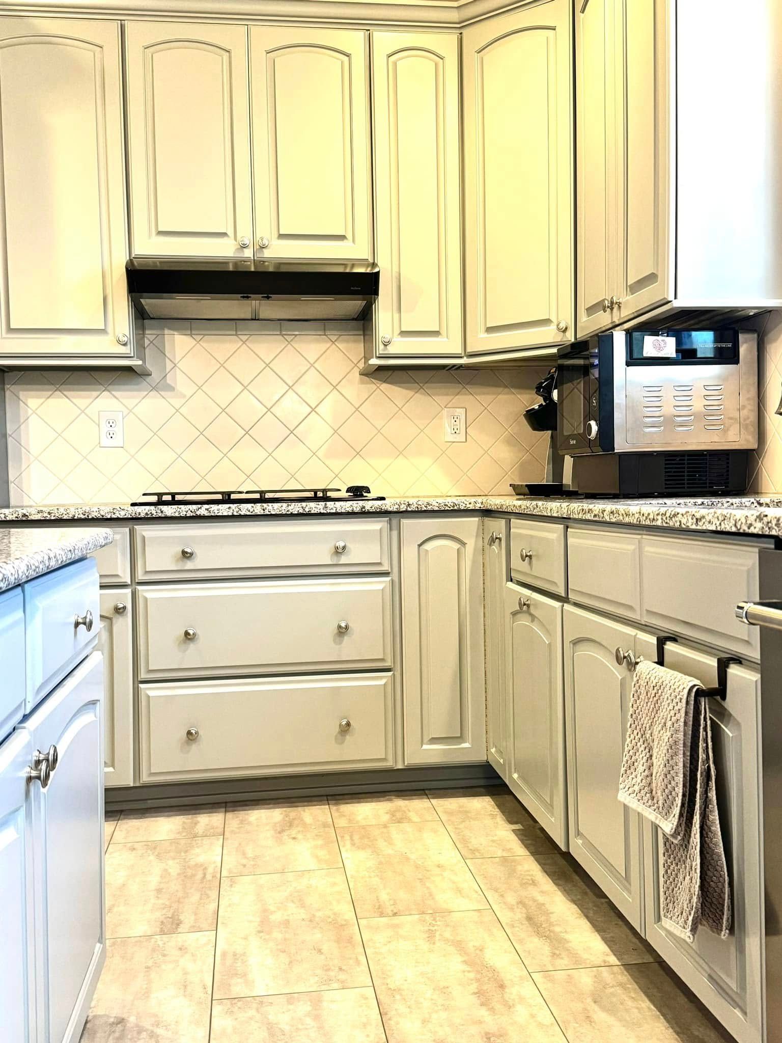 Bright cream kitchen with white cabinets, granite counters, tiled backsplash, and a built-in oven.