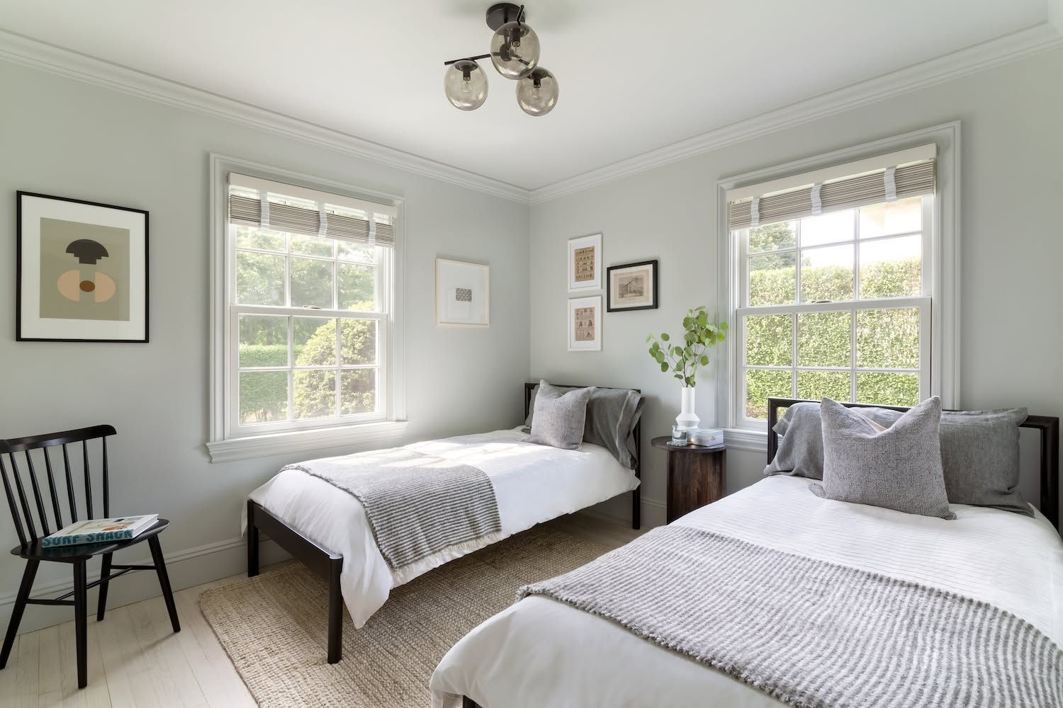 Bright bedroom with two twin beds, gray bedding, white walls, and large windows letting in daylight
