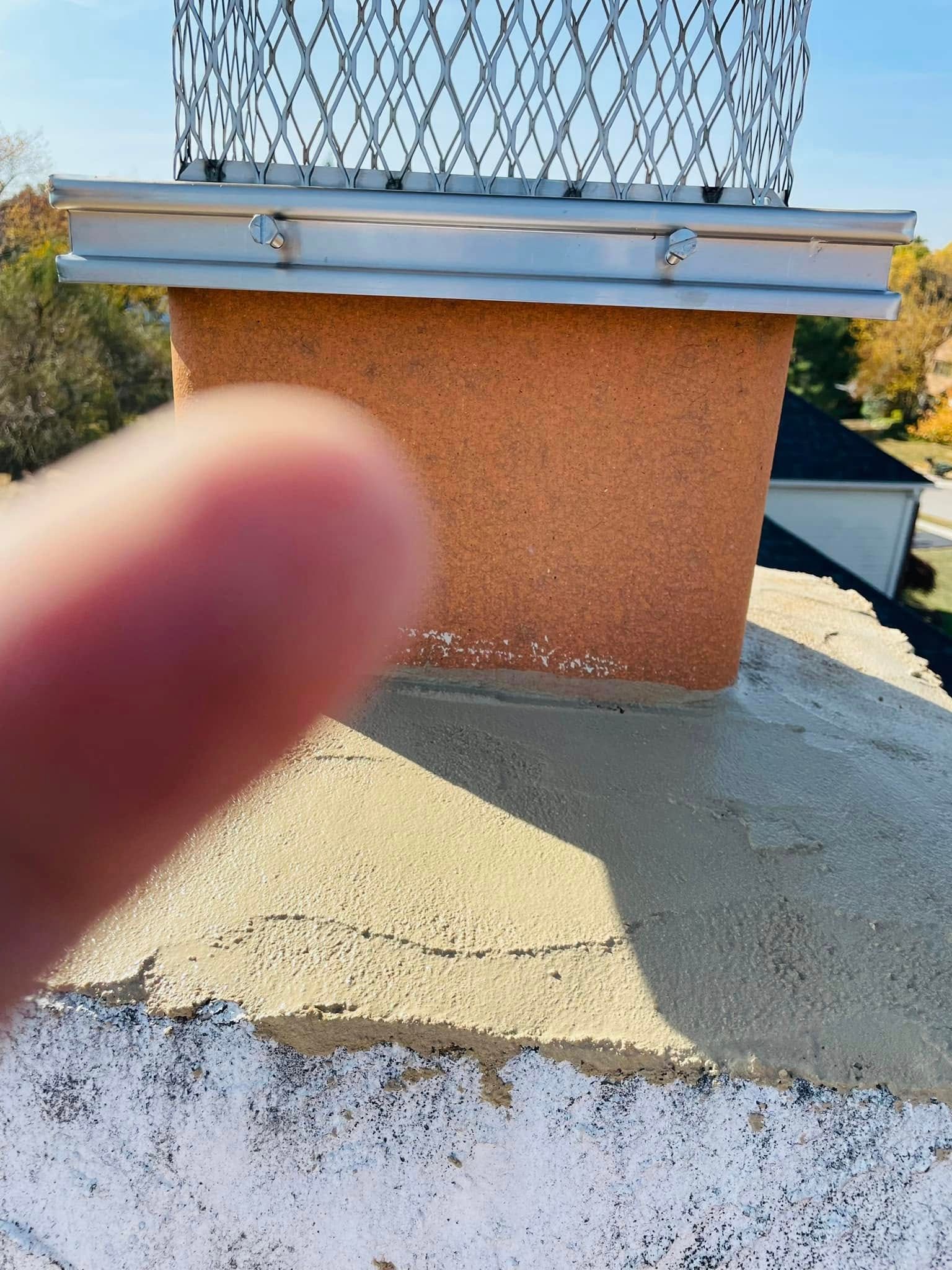 Finger pointing at a rooftop chimney with orange stucco and metal flashing under a wire mesh cap