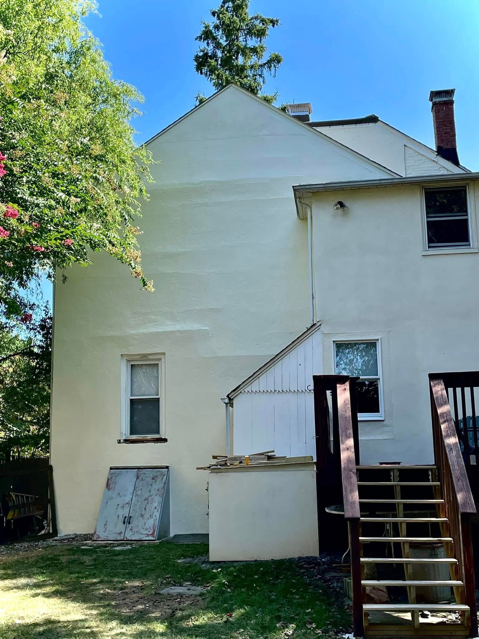 Back of a white house with stairs, porch, and trees in a sunny yard
