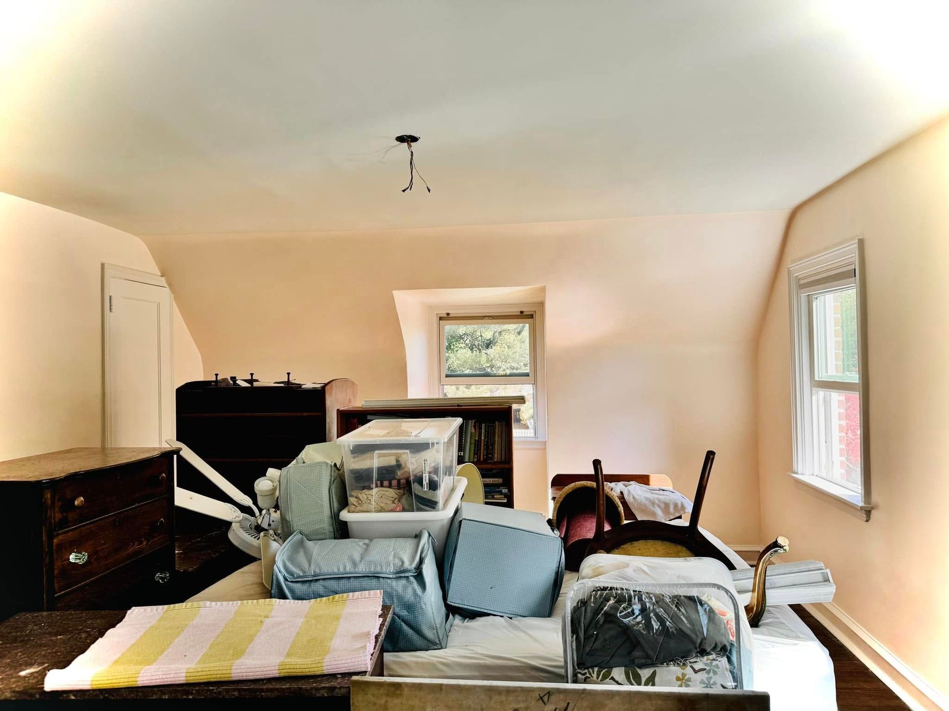 Cluttered living room with furniture piled and covered in plastic under a windowed, sloped ceiling