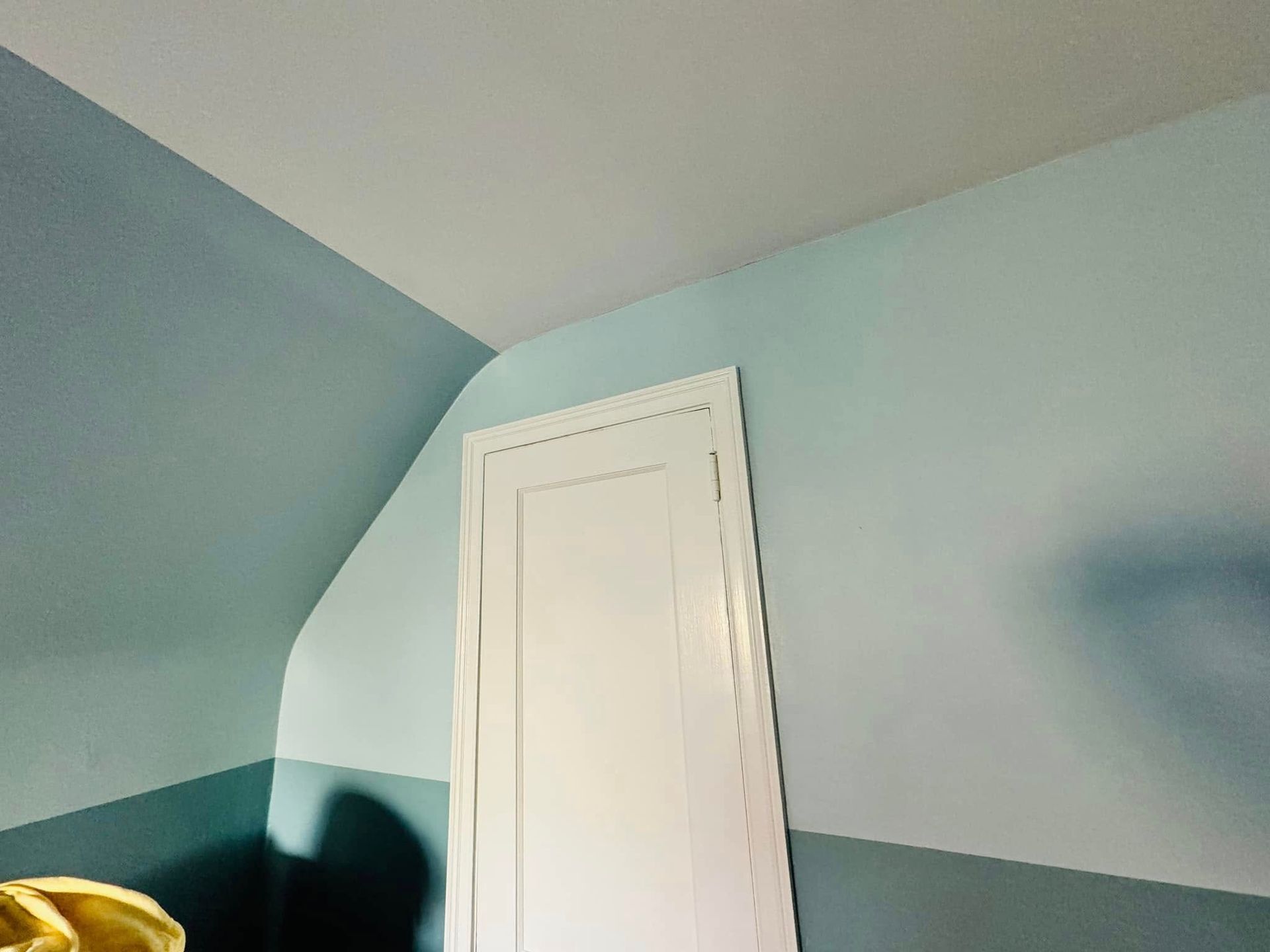Corner of a light blue room with a white door and dark furniture edge in the foreground