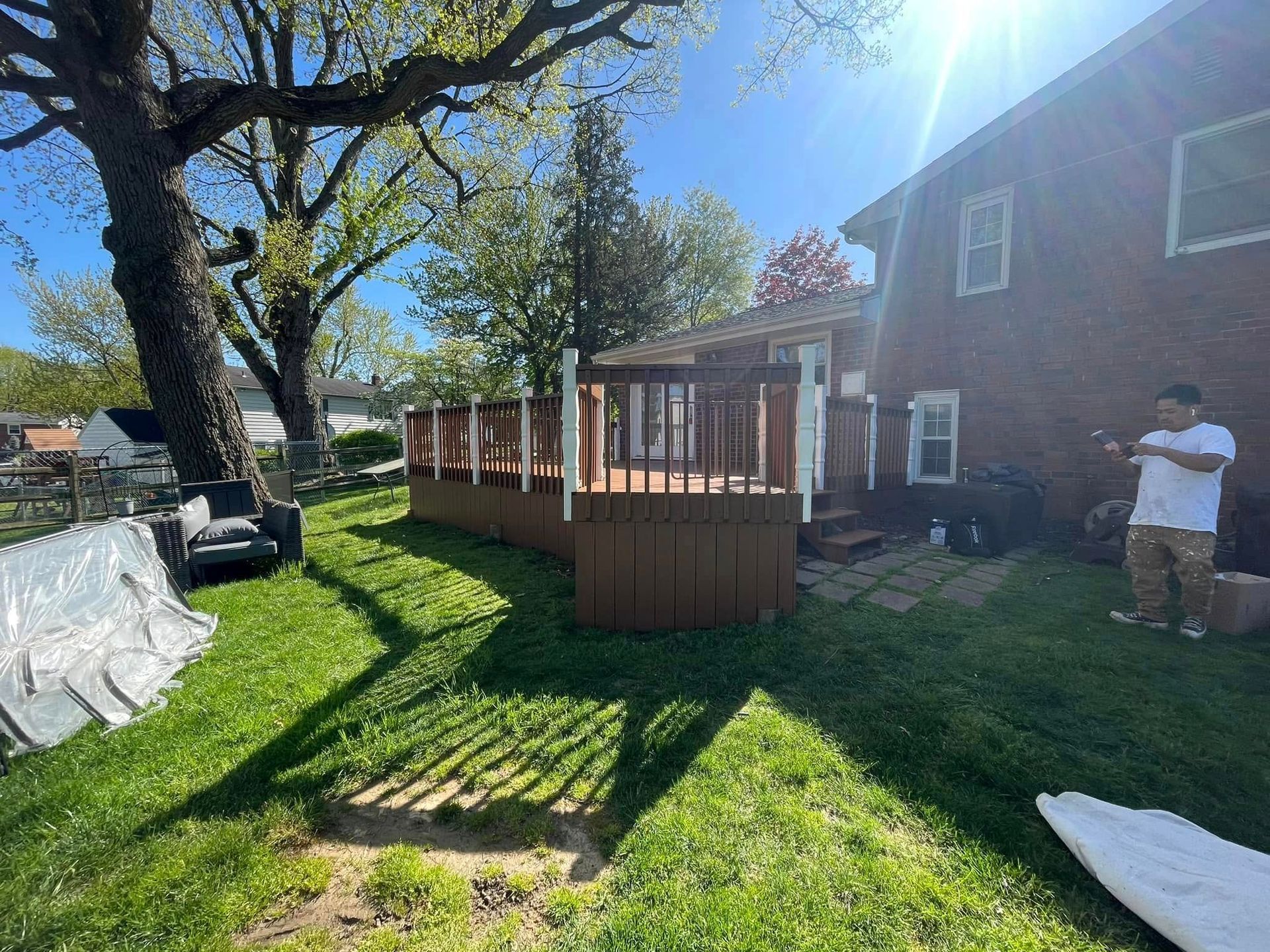 Backyard with a wooden deck under construction beside a brick house on a sunny day