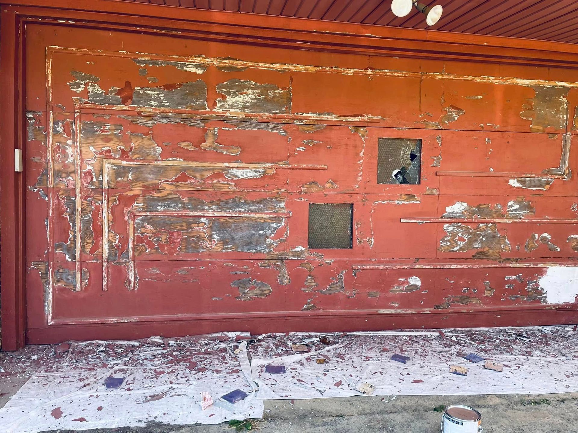 Weathered red garage door with peeling paint and two small square openings