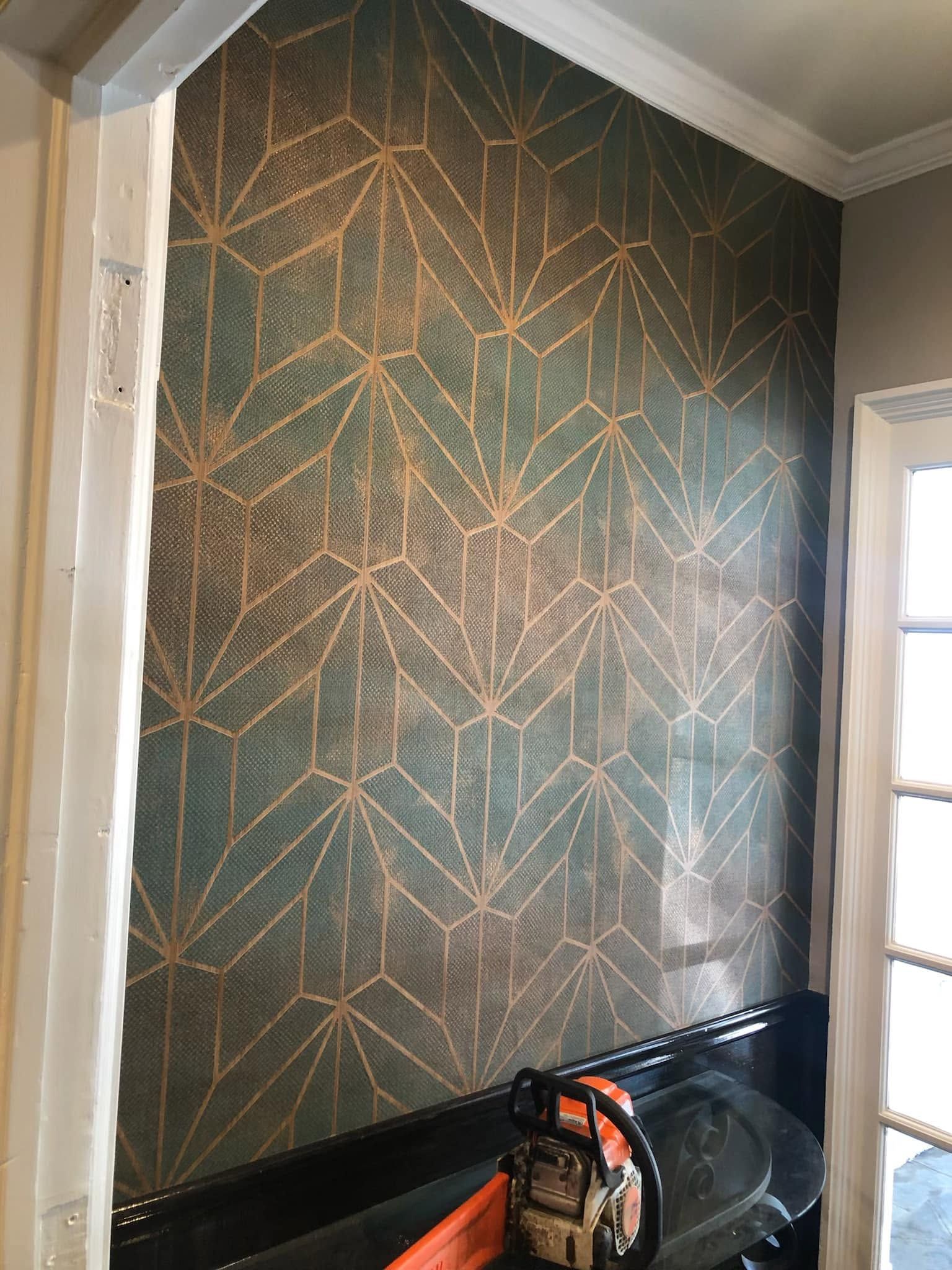 Partially painted wall with gold geometric lines over dark green paint in a room under renovation