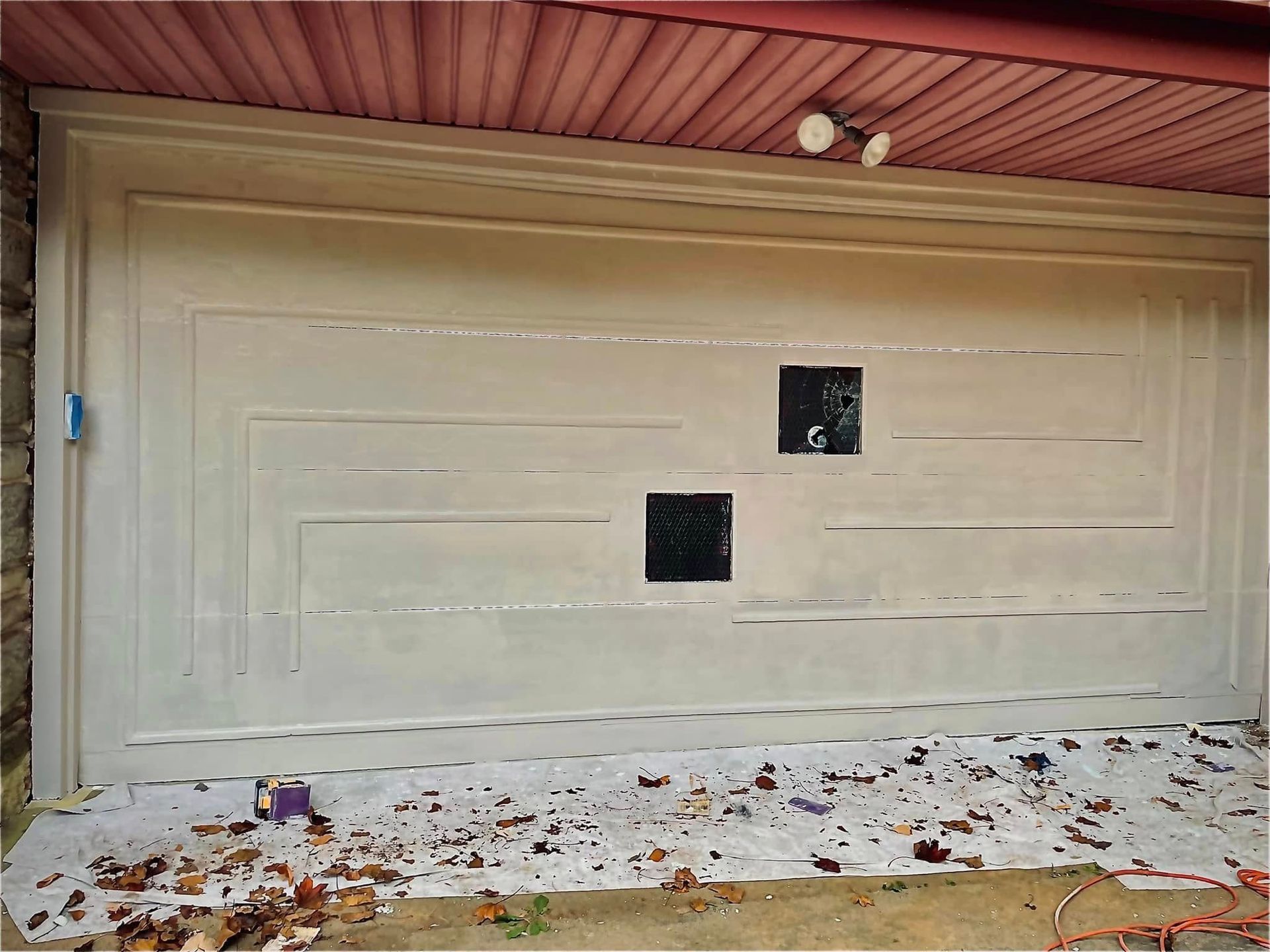 White garage door with two small square windows, covered in scattered leaves under a red porch ceiling