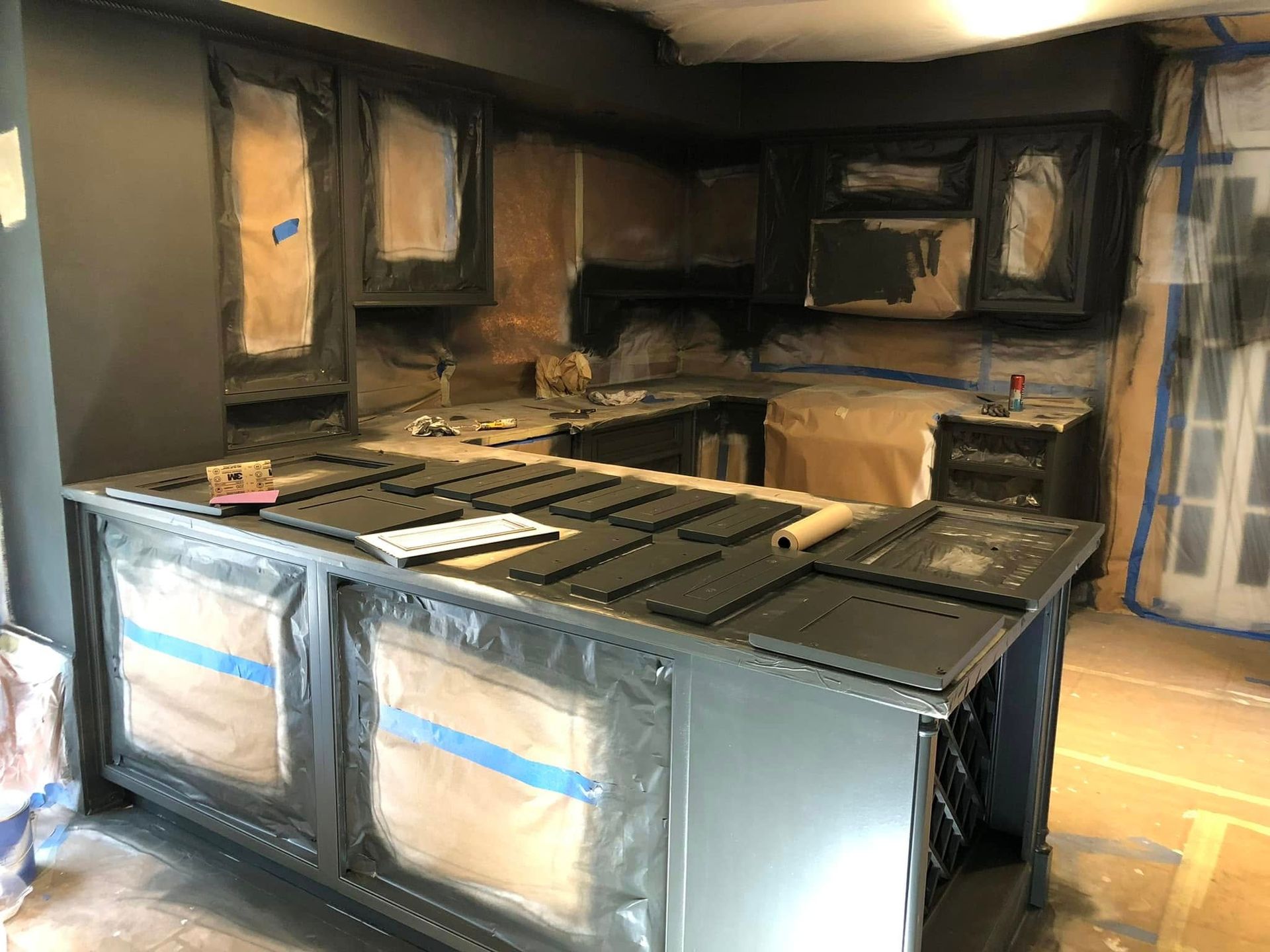 Kitchen cabinets under construction with dark finishes, taped fronts, and unfinished countertops in a renovated kitchen.