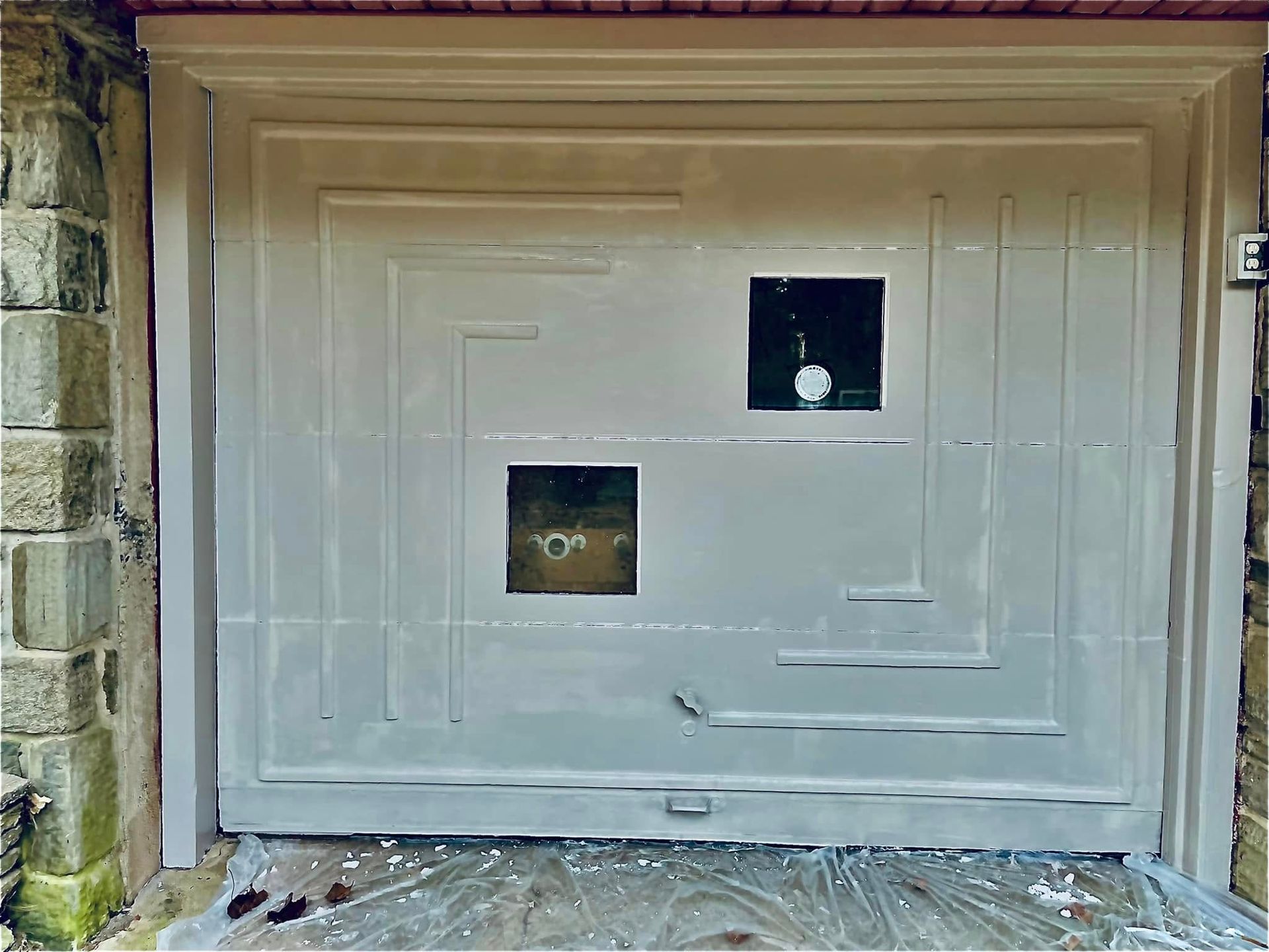 White garage door with two small square windows and a decorative panel pattern in a stone doorway.