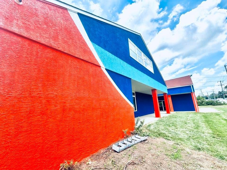 Bright red and blue building exterior with sloped walls and a grassy path under a partly cloudy sky