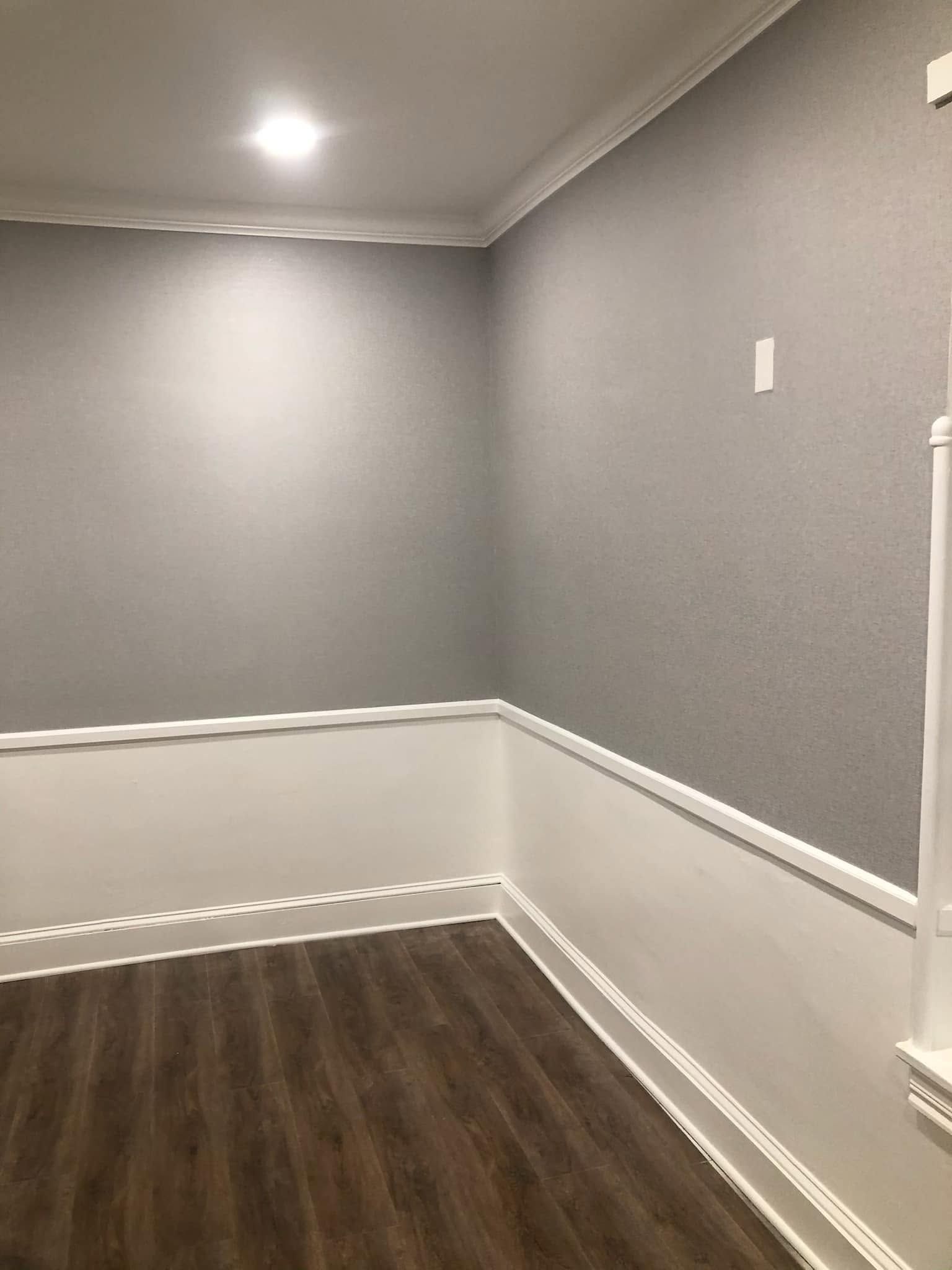 Empty gray room with white wainscoting, dark wood floor, and recessed ceiling light.