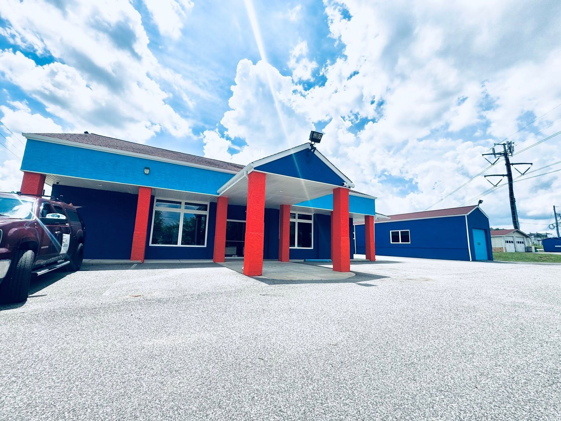 Colorful roadside building with blue roof, red pillars, and parked vehicles under a bright sky