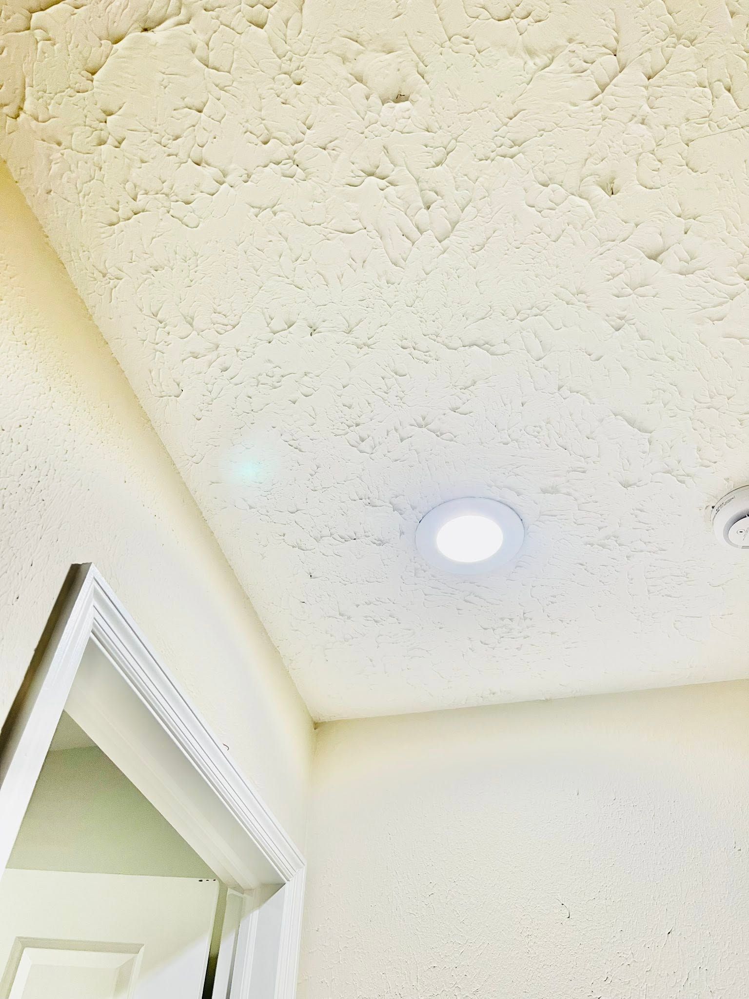 White textured ceiling with a recessed light above a doorway corner