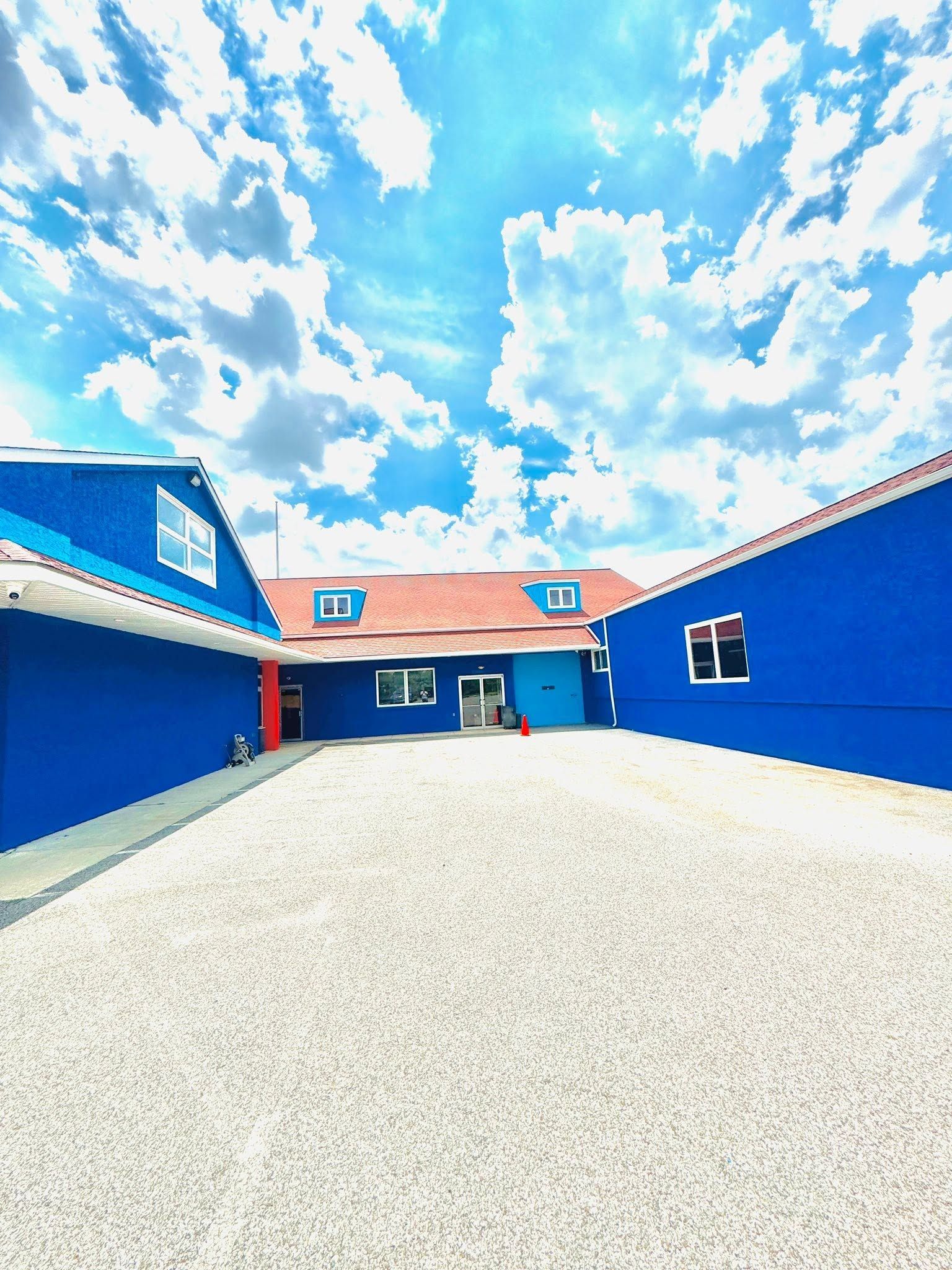 Blue courtyard between buildings under a bright sky with scattered clouds.