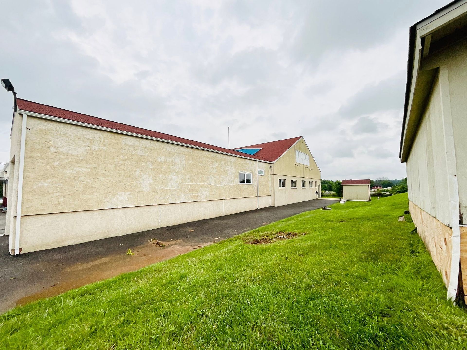 Long beige building with a red roof beside a grassy path under a cloudy sky