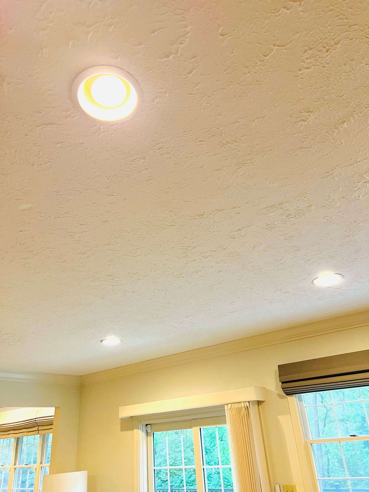 Ceiling with recessed lights above large windows and blinds in a bright room