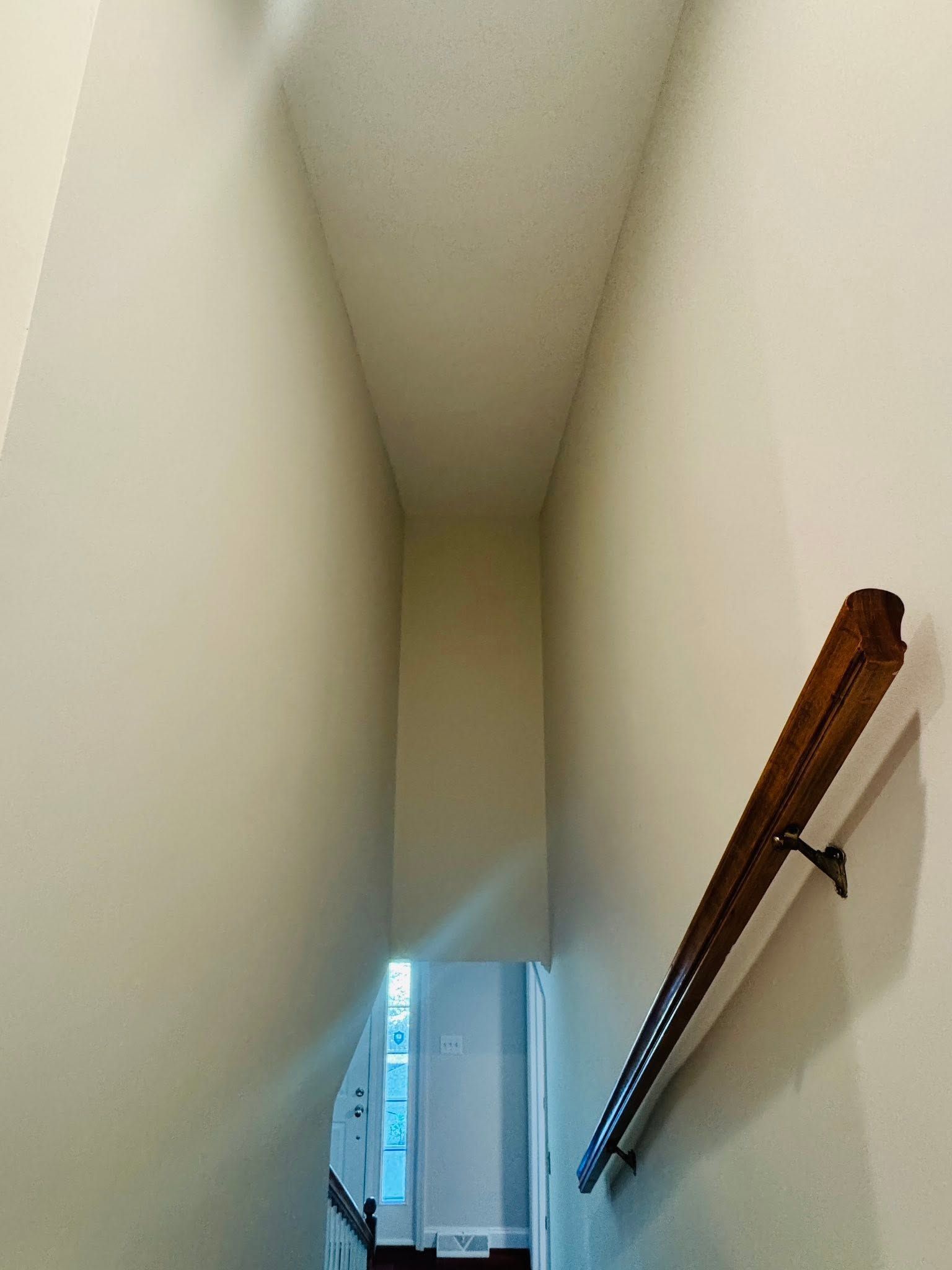 Narrow staircase landing with cream walls, white ceiling, and a wooden handrail on the right.