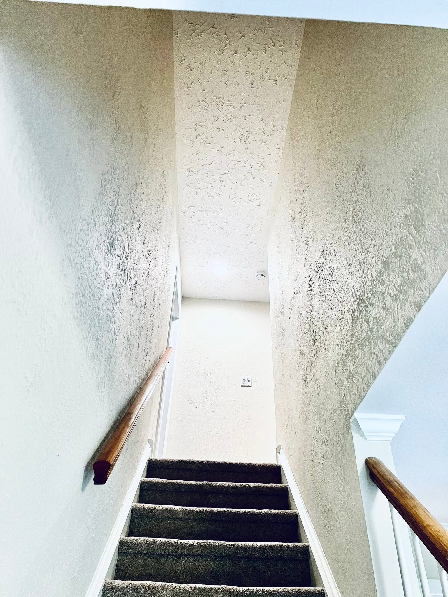 Staircase looking up to a bright landing, with speckled walls and wooden handrails on both sides.