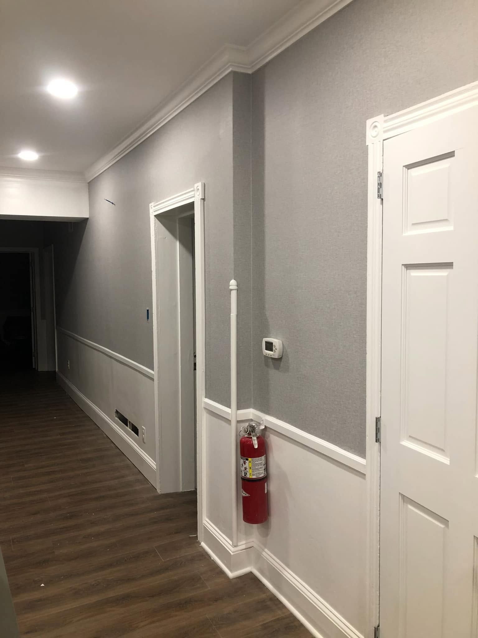 Empty hallway with gray walls, white trim, wood floor, and a fire extinguisher on the wall