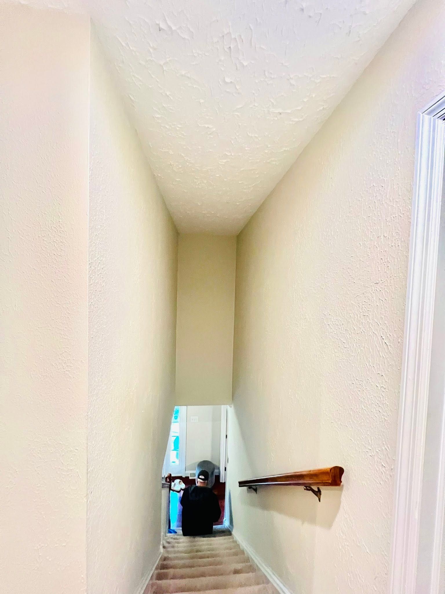 Narrow beige hallway with a brown handrail and a person at the far end near a bright doorway