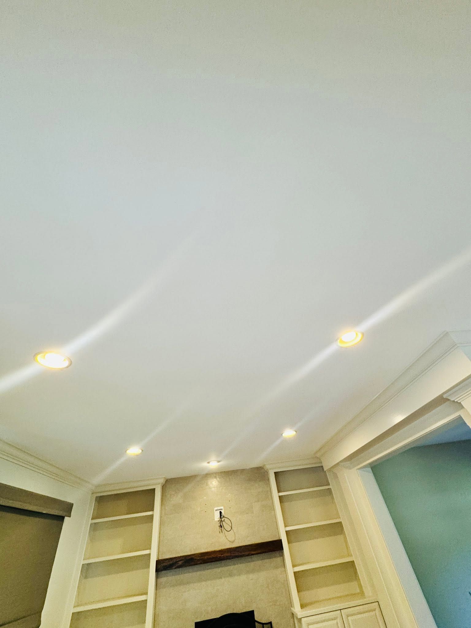 Ceiling with recessed lights above built-in white shelves and a mantel in a room