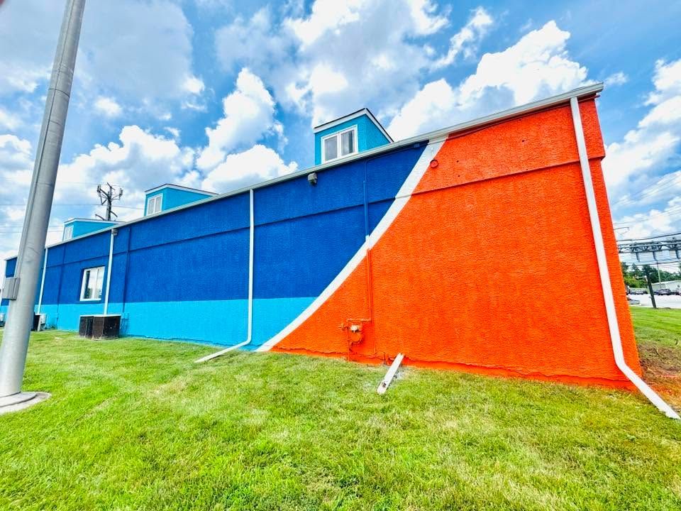 Bright blue and orange building wall on a grassy field under a cloudy sky
