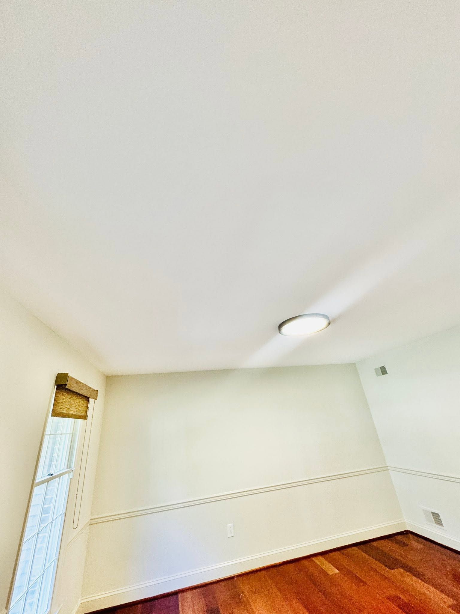 Empty white room with beige carpet, a ceiling light, and a tall window with blinds