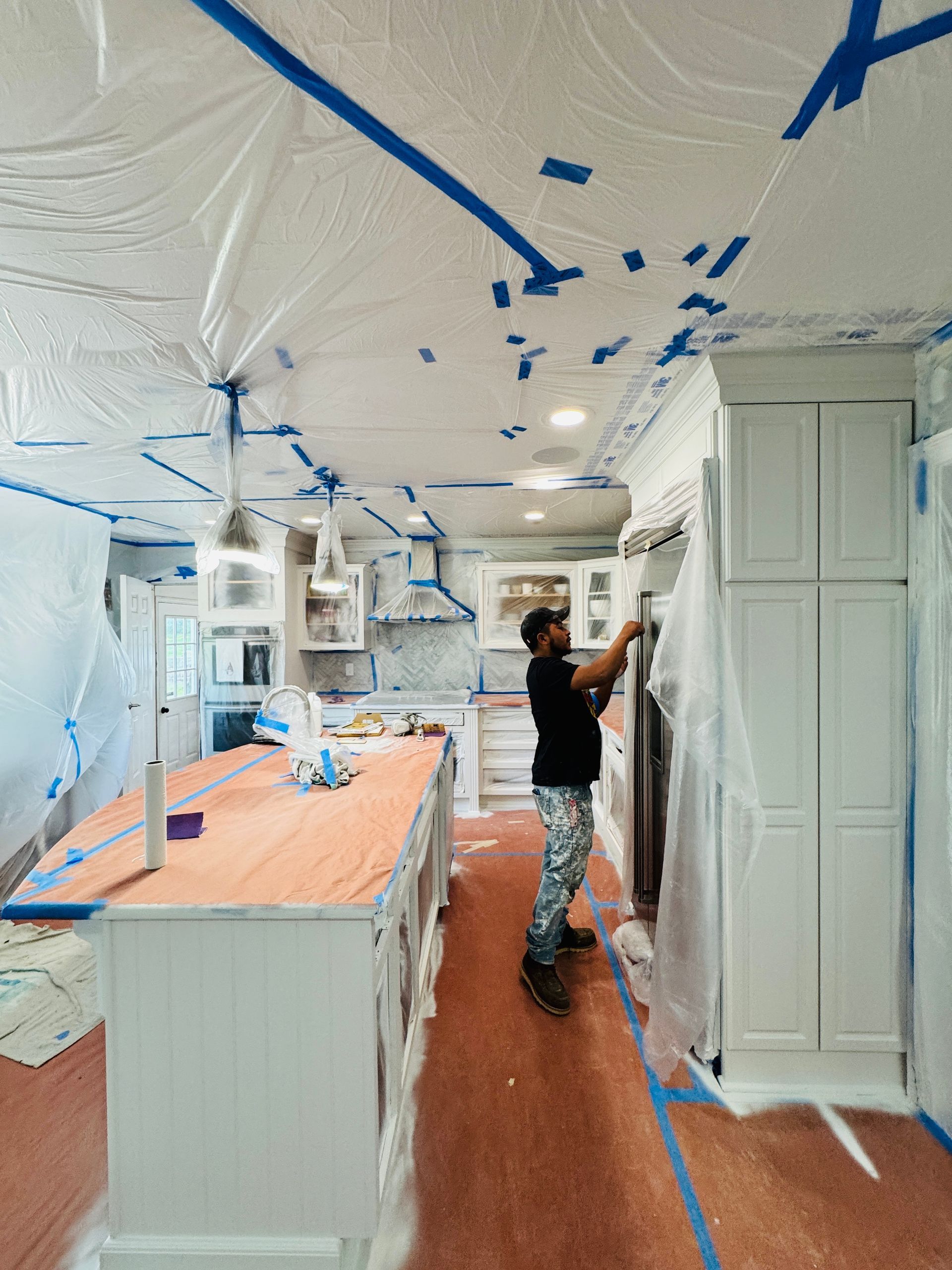 Person painting a kitchen ceiling and cabinets with blue tape protecting surfaces