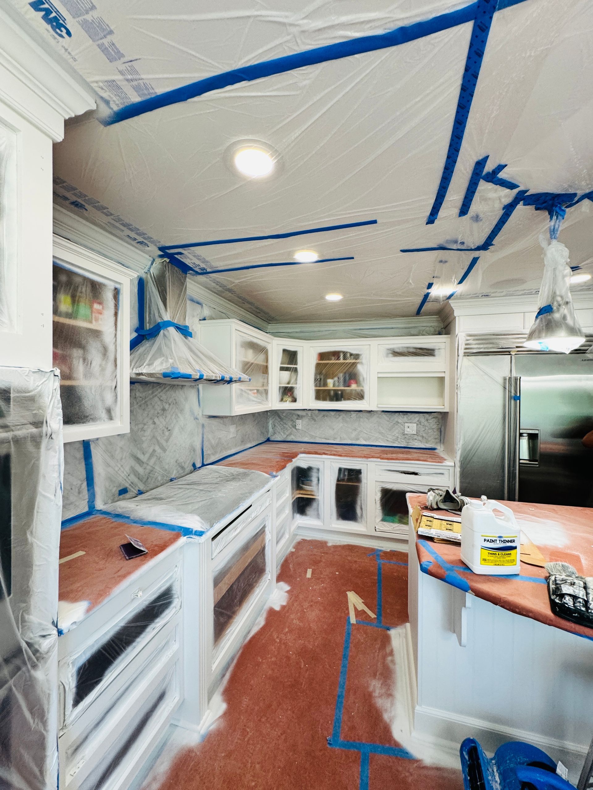 Kitchen under renovation, with cabinets and ceiling taped off for painting or repairs.
