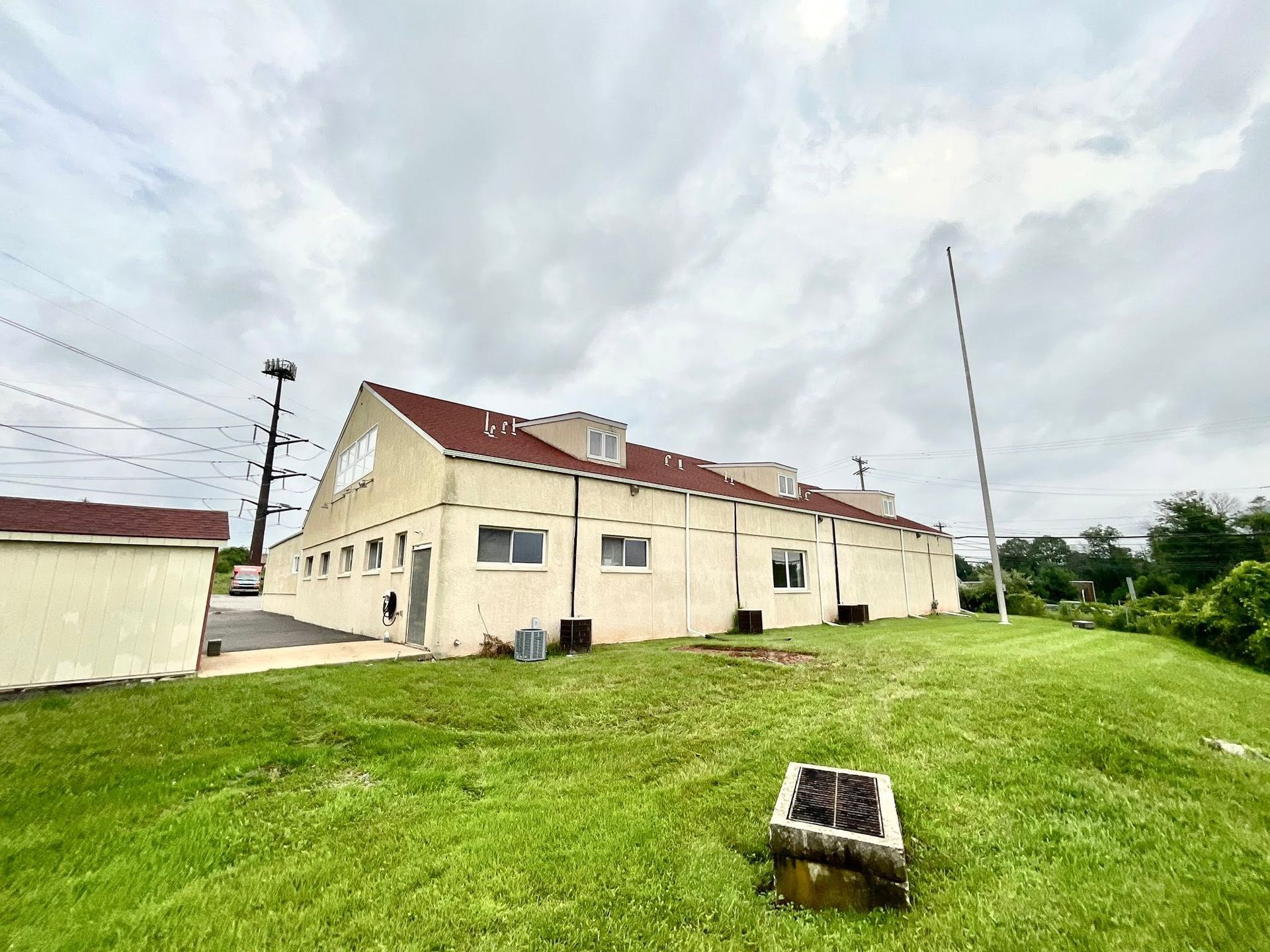 Cream-colored building with a red roof on a grassy hill under a cloudy sky